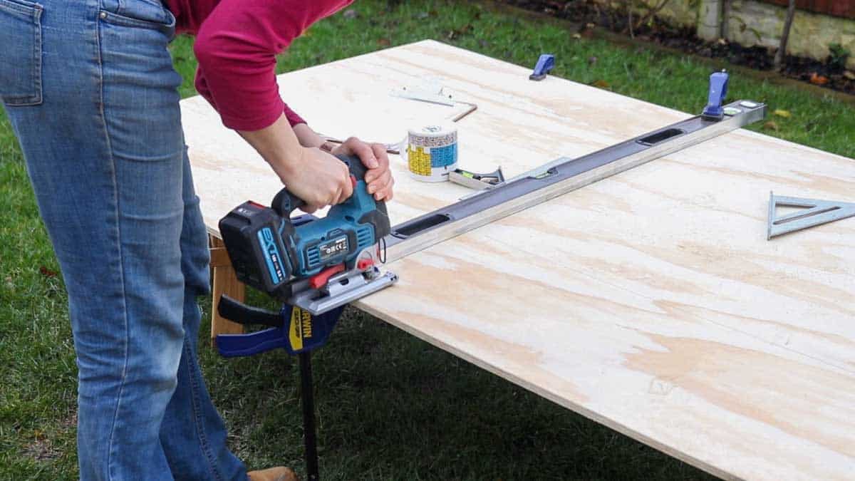 cutting a plywood corner shelf using a jigsaw and a clamped straight edge