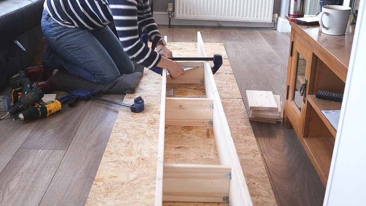 Using clamps and a right angle before screwing DVD storage supports between shelves