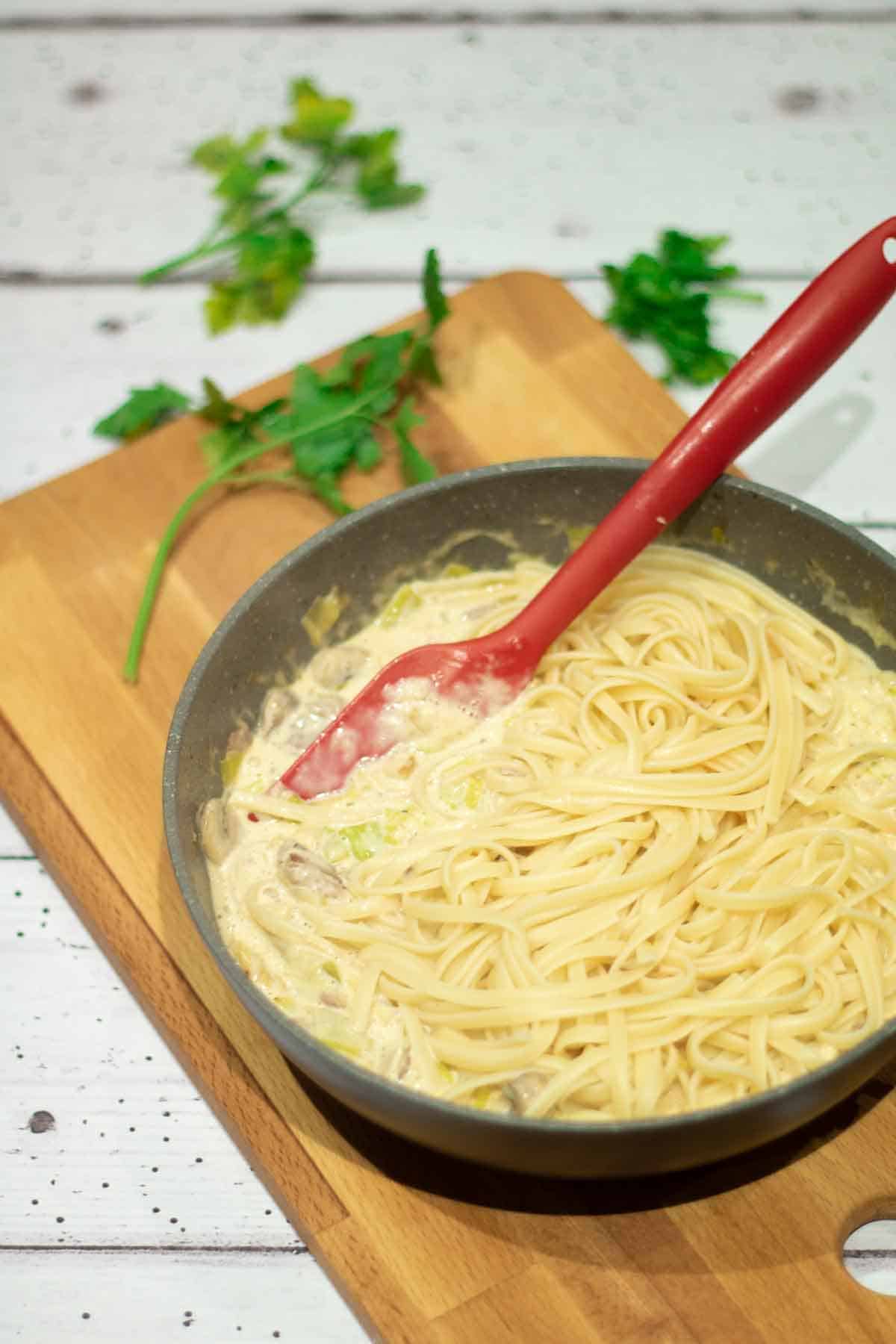 leeks and cream getting mixed together with linguine in a large deep frying pan