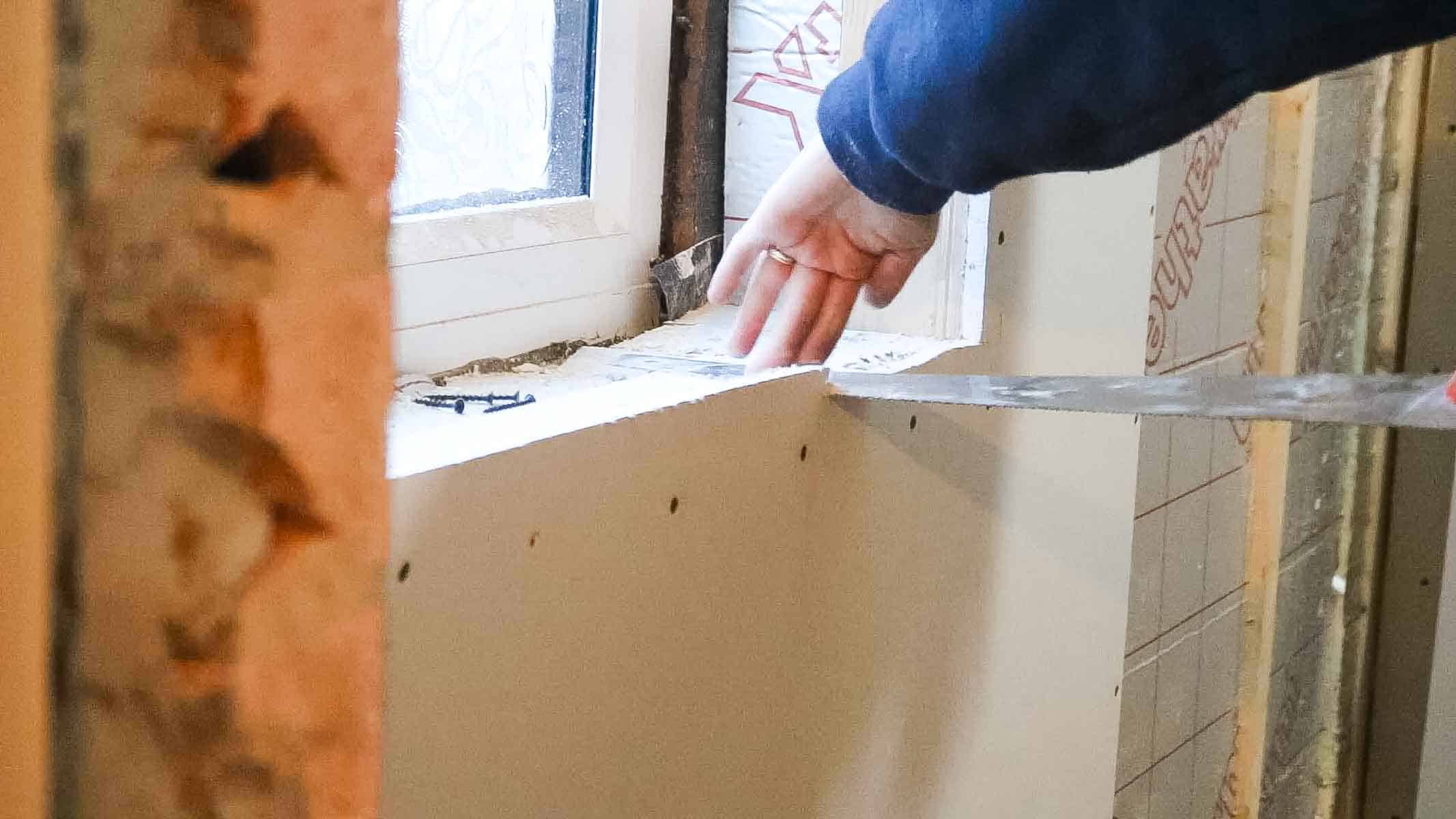 cutting plasterboard around the window with a hand saw