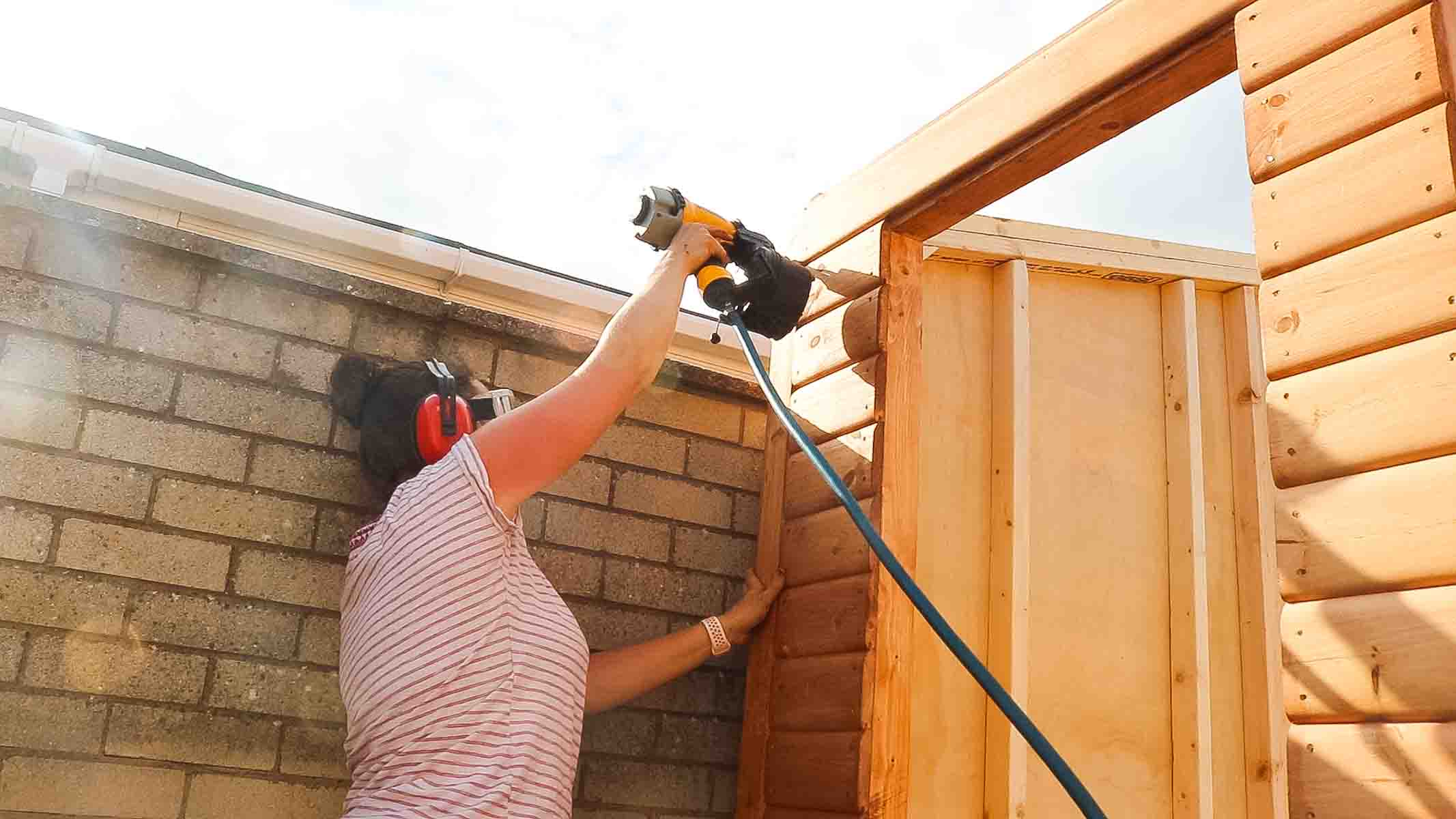 Female woodworker nailing cladding trim on the corner of a summer house