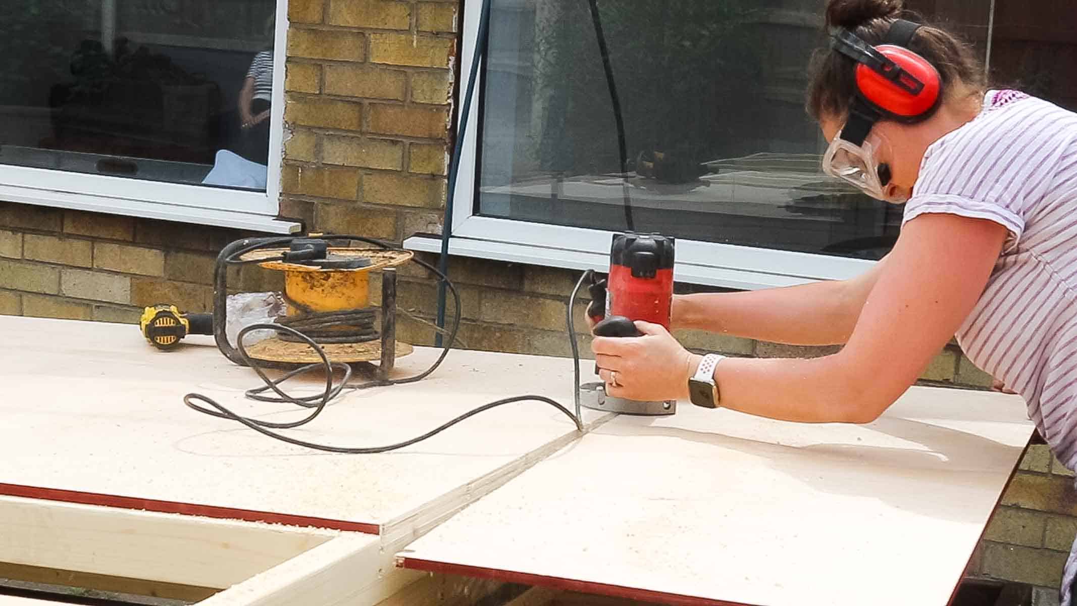 The Carpenter's Daughter trimming off plywood cladding excess with a flush trim router bit
