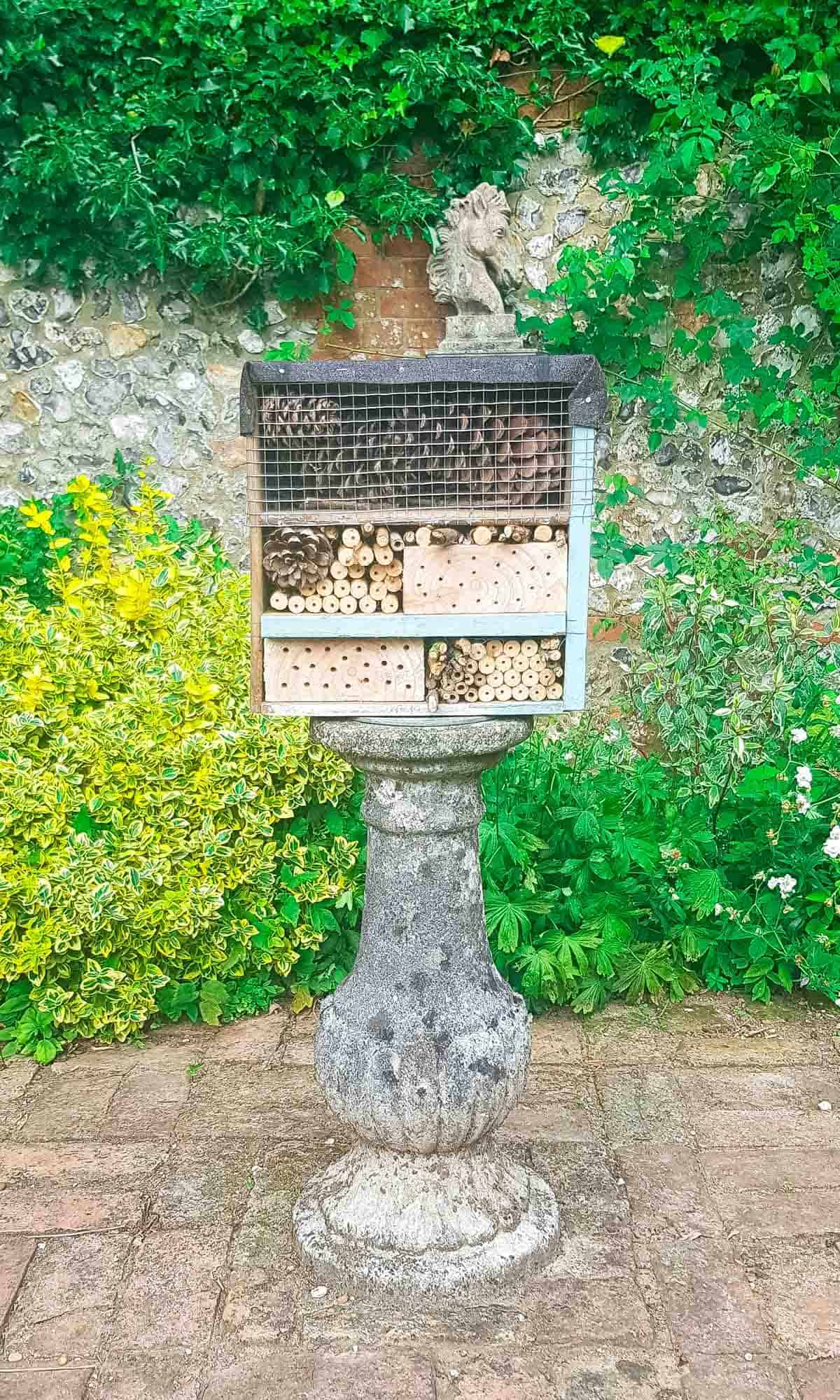 Bee and bug house on a sun dial stand, surrounded by flowers, plants for a productive garden