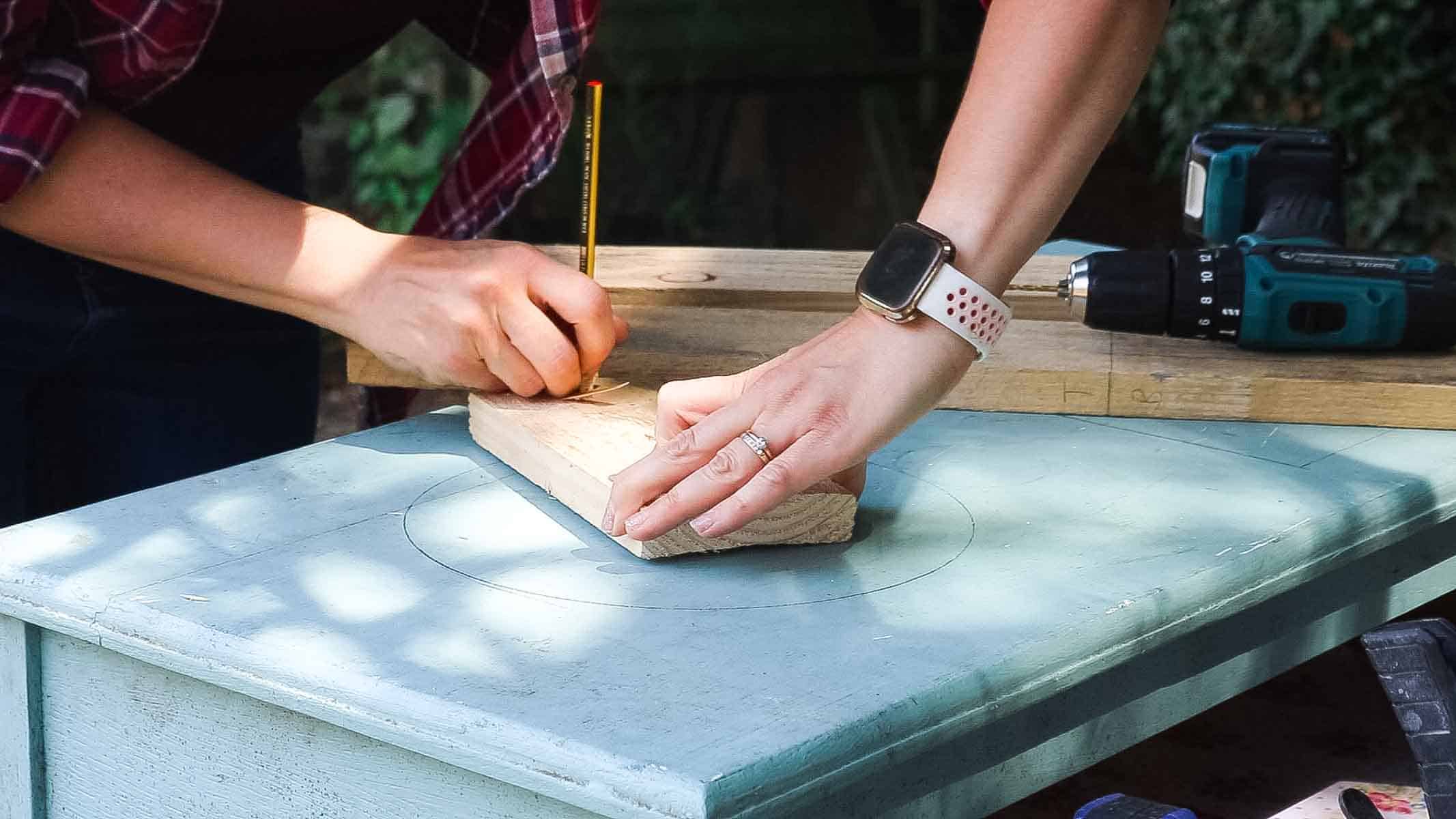 Female carpenter working on DIY kitchen crafts by drawing a perfect circle on top of an old chest of drawer to cut for a washing up bowl