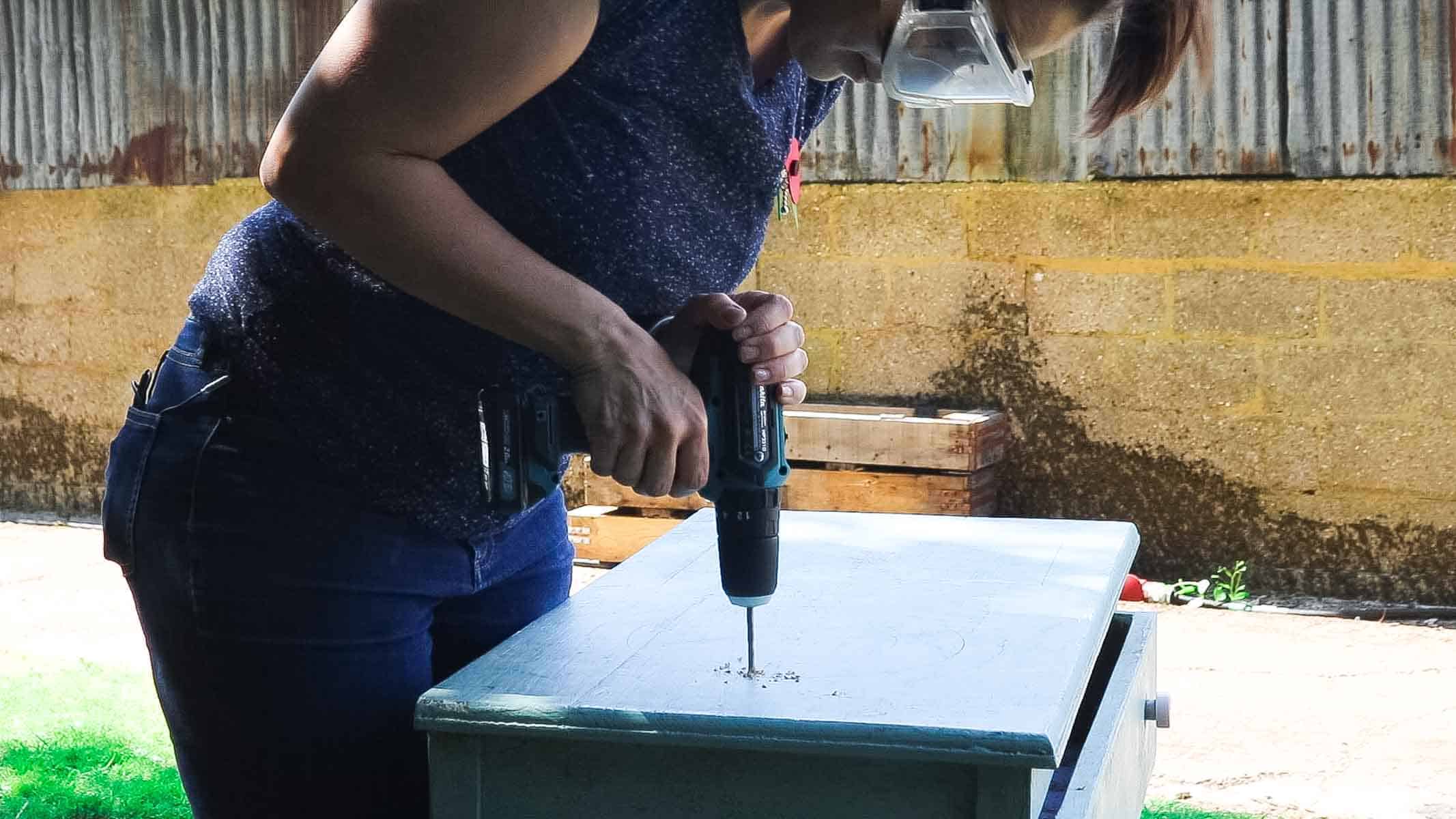 Woman drilling a hole before cutting with a jigsaw for a round washing up bowl in a DIY country kitchen for outside