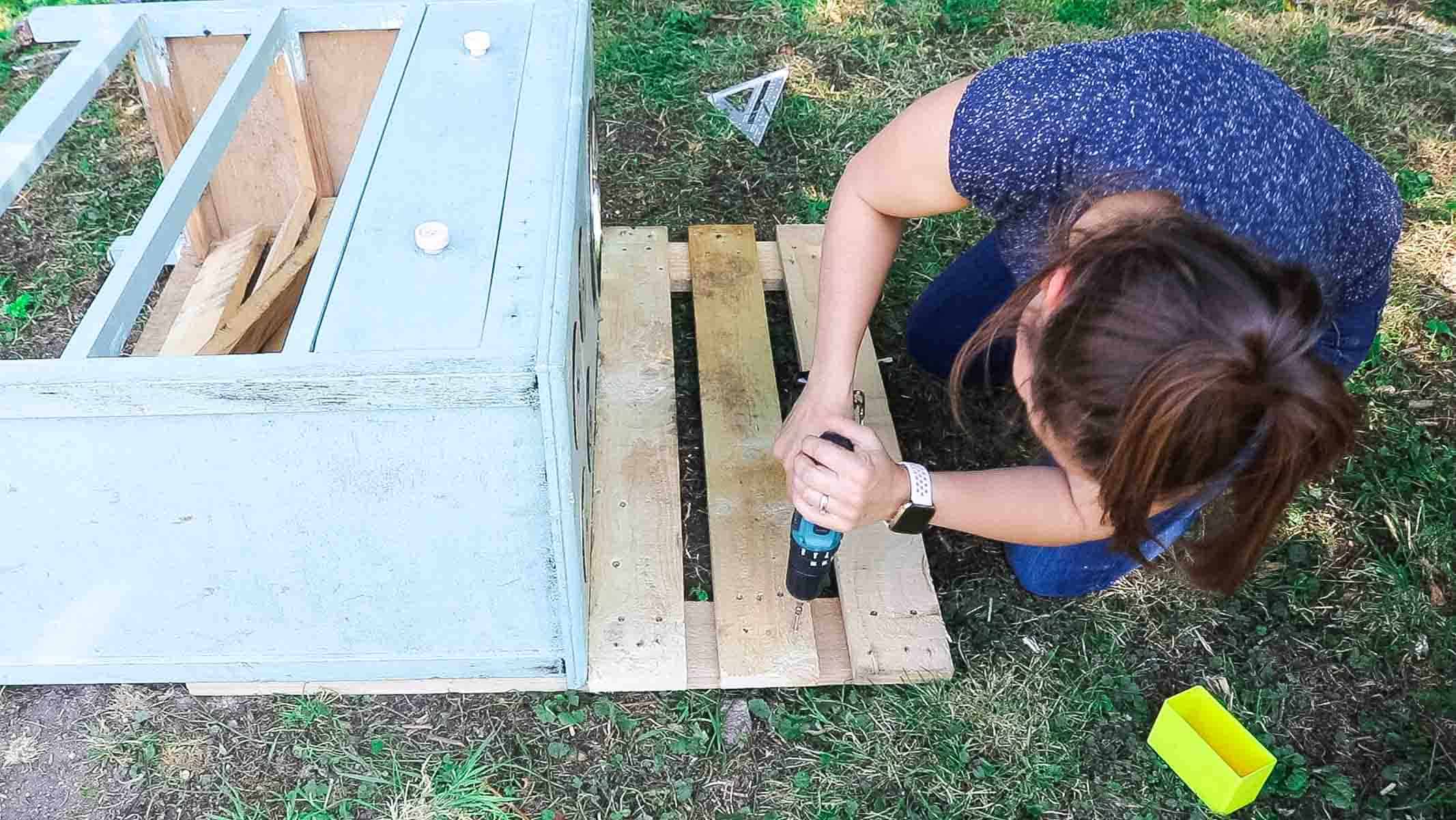 Woman making mud kitchen from pallets as a backing on some old drawers