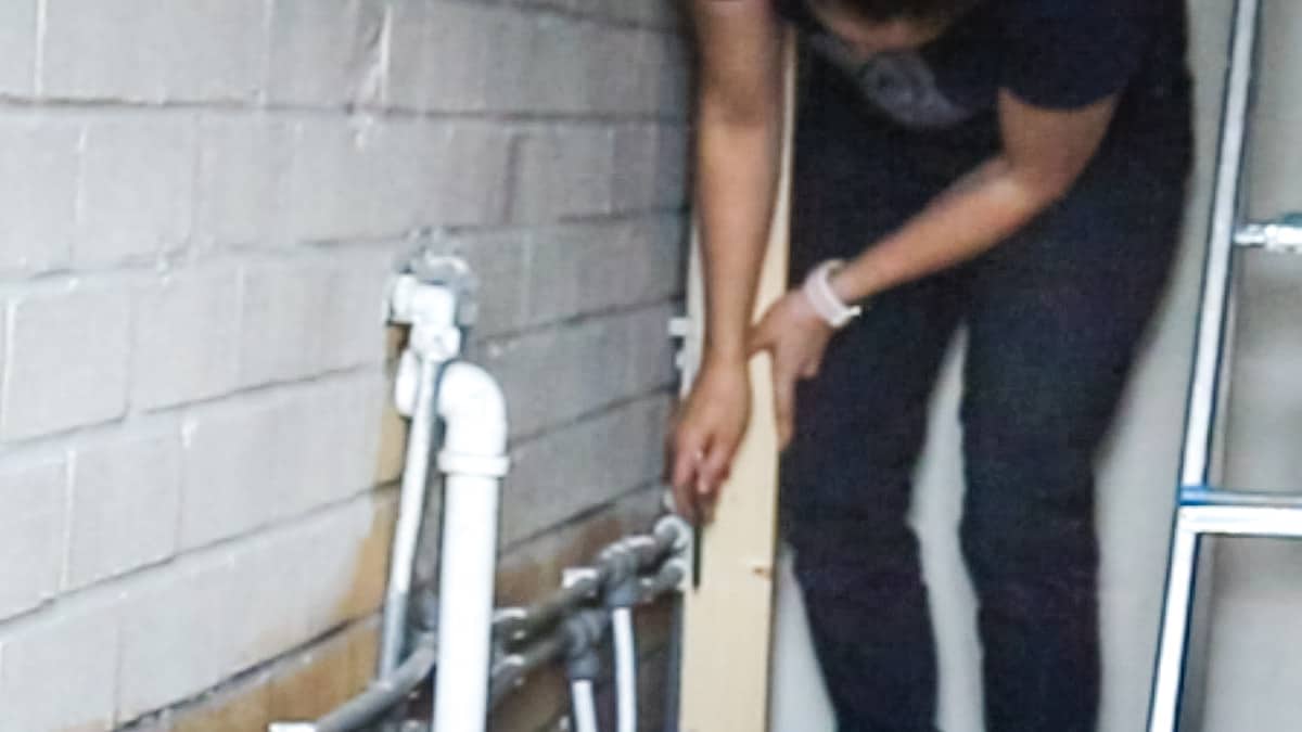 Woman drawing around pipes on structural timber to cut out a notch