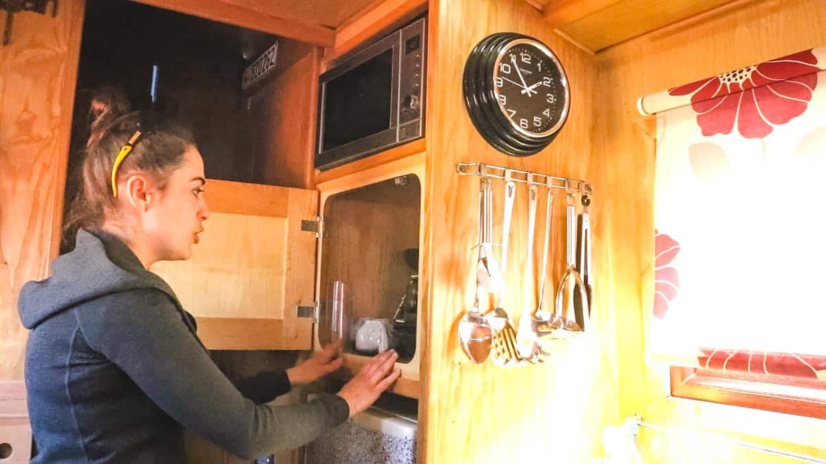 Woman opening narrowboat kitchen cupboard above fridge