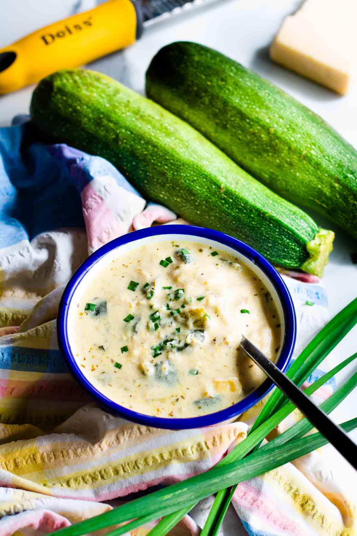 Bowl full of Keto creamy cheesy courgette soup in Falcon enamel bowl on white marble worktop.