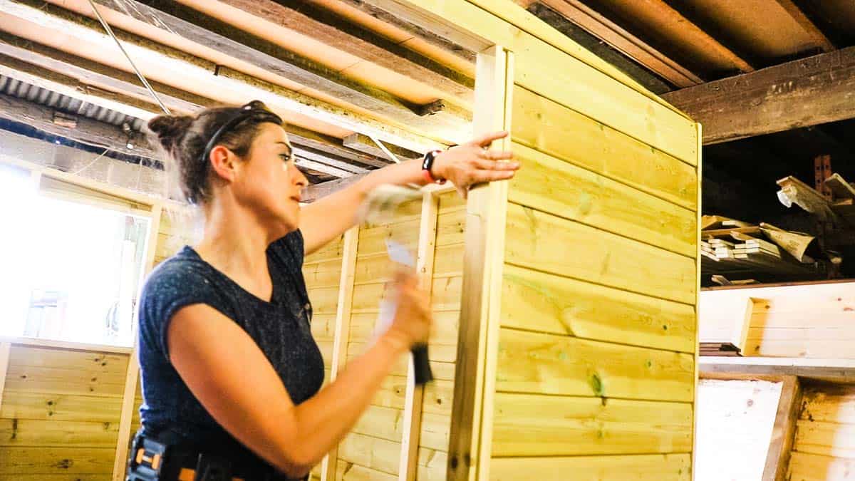 Woman nailing shed door trim on opening