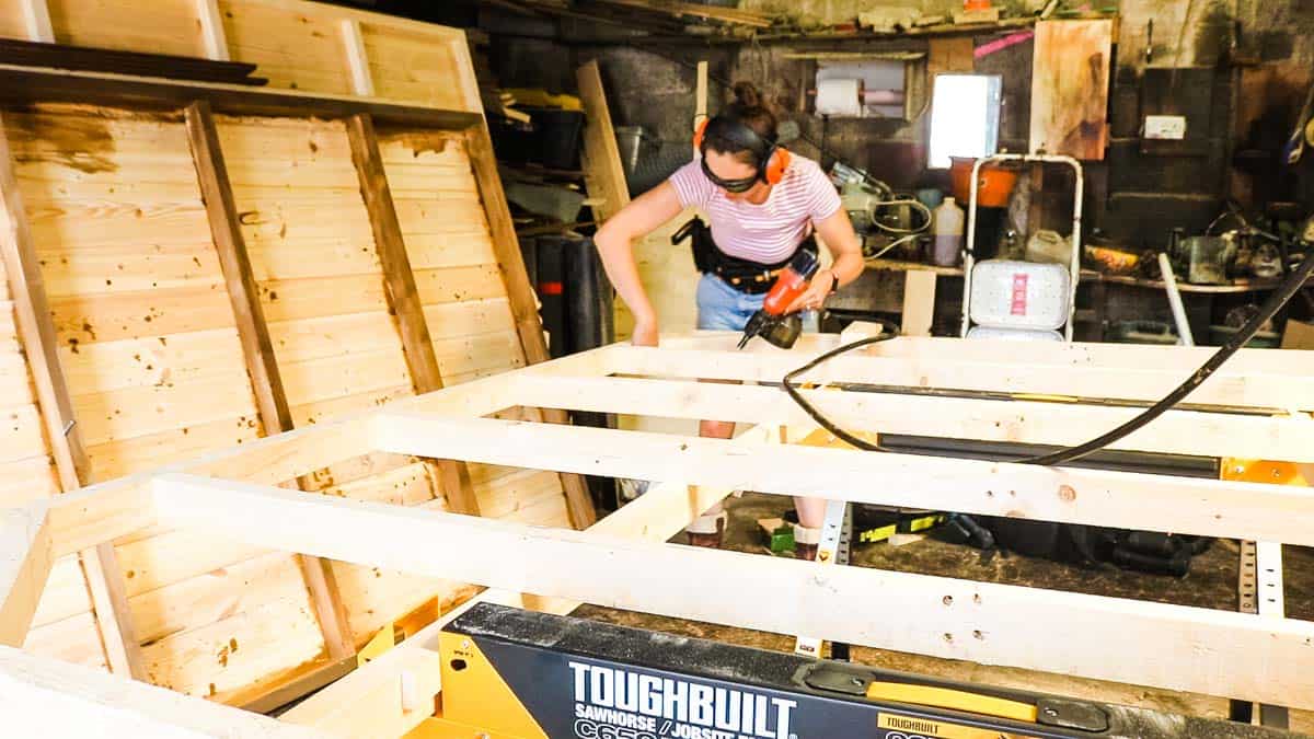 Woman nailing mitred offcuts in the corner of shed base to keep square