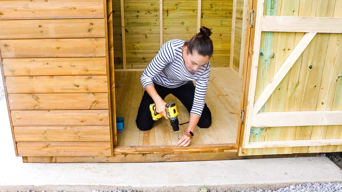 Woman building a shed and screwing to base on concrete foundations