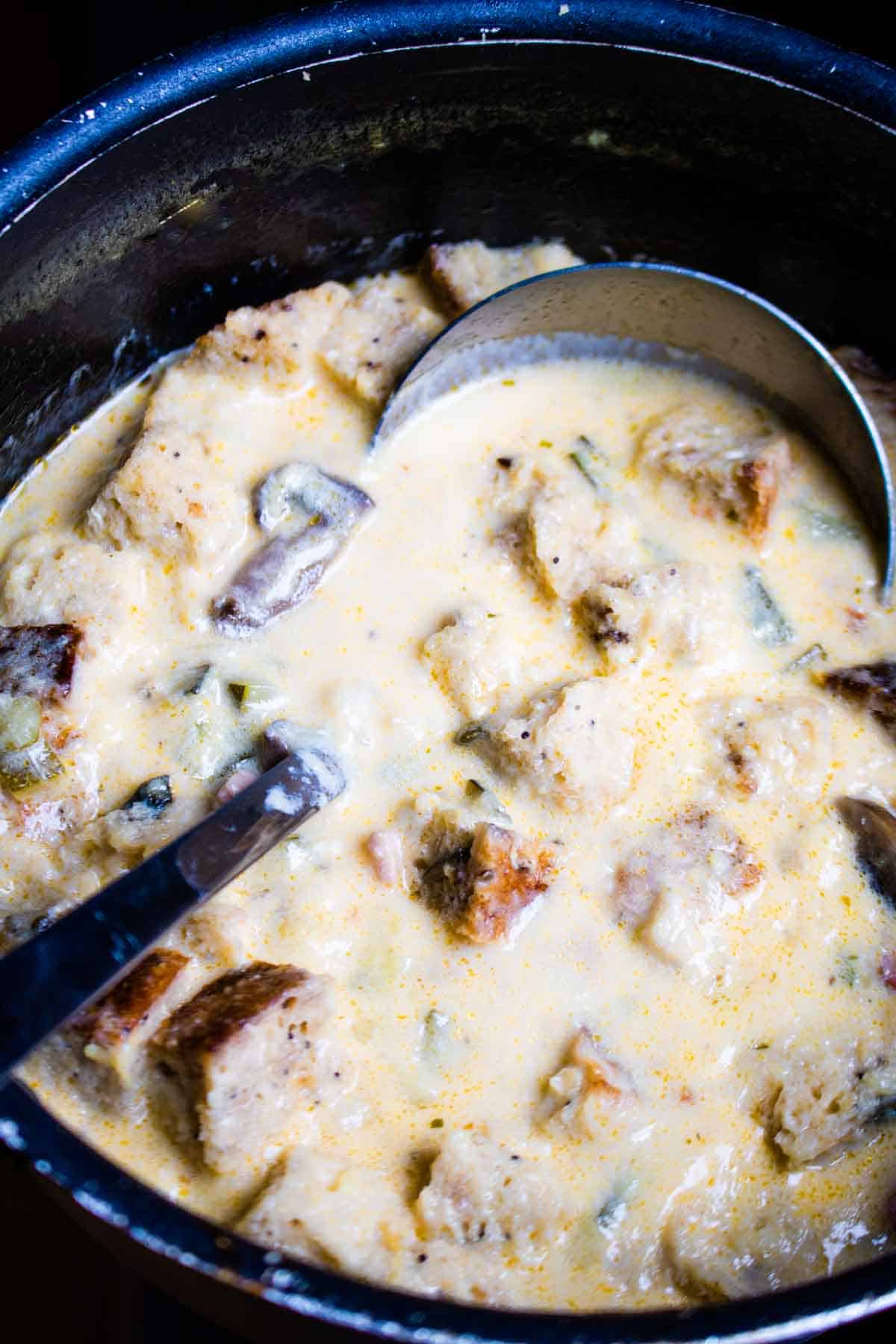 Close up of a ladle in a pan of cheesy bacon soup with York bread chunks.