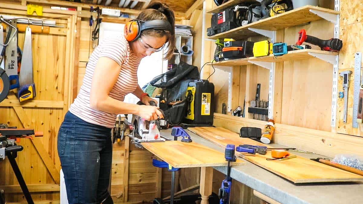 Woman cutting wood with a circular saw in workshop