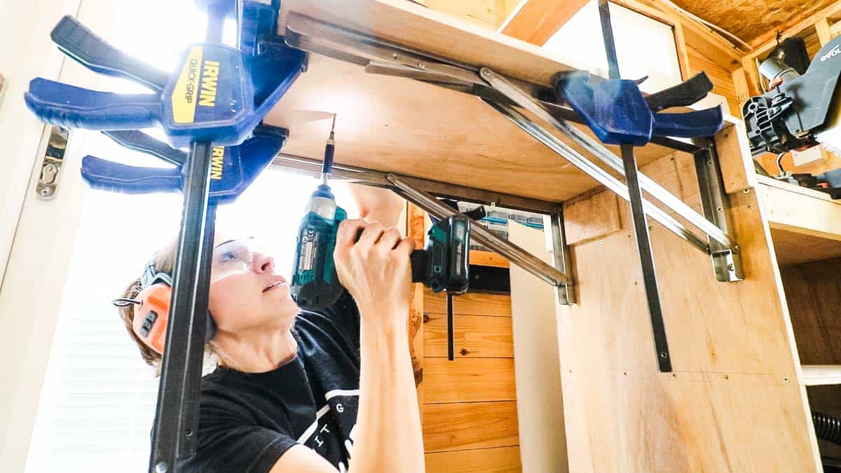 woman screwing folding metal brackets for a collapsible shelf