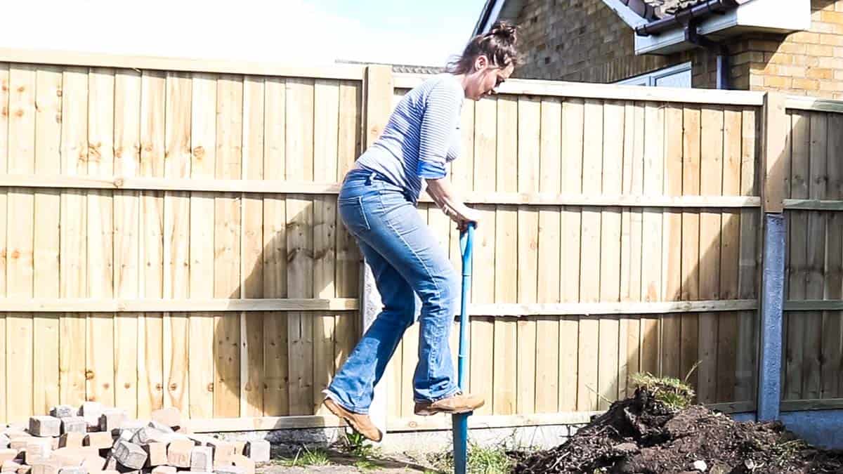 woman digging a trench to install railway sleepers in the garden