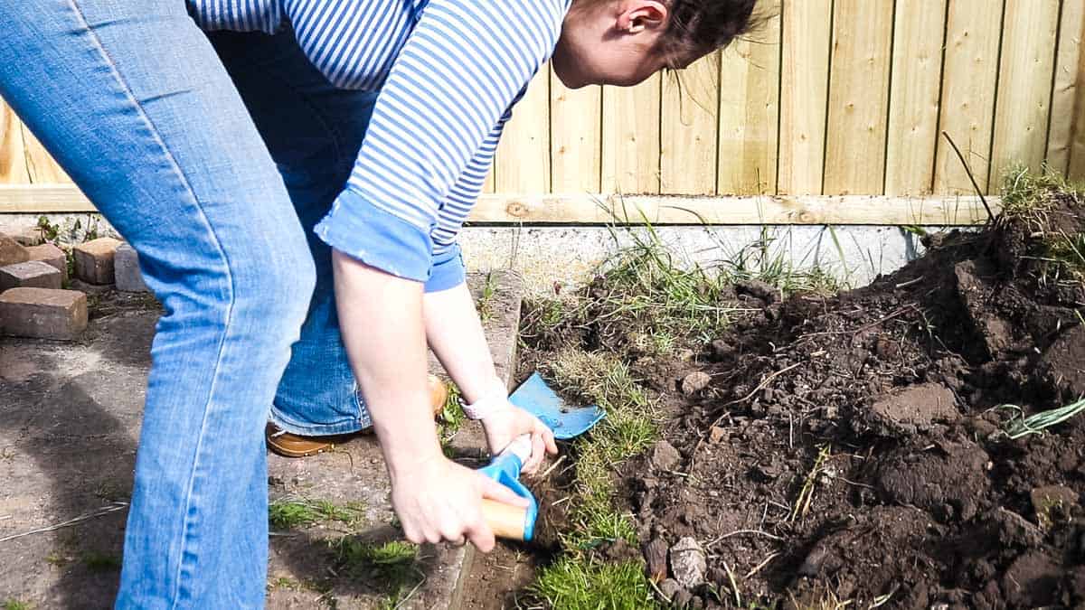 woman removing top soil from trench in garden