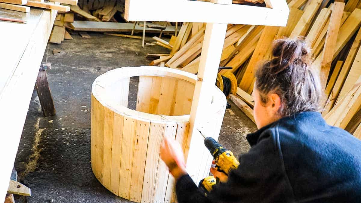 woman screwing roof posts to a wooden well base