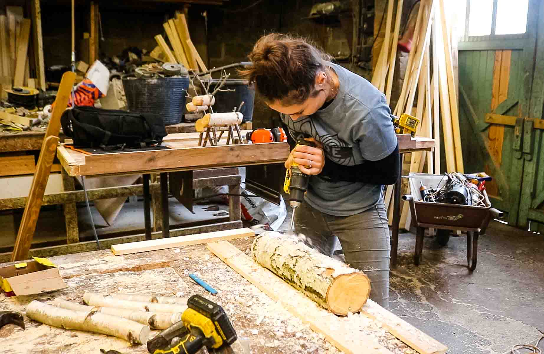 Female carpenter drilling holes in a silver birch log for reindeer legs
