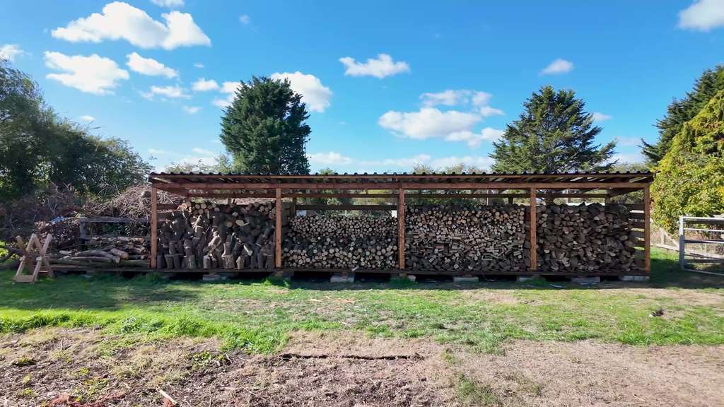 Our completed long timber log store filled with firewood beneath its metal roof.