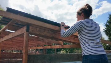 Positioning a metal roofing sheet over the timber roof supports.